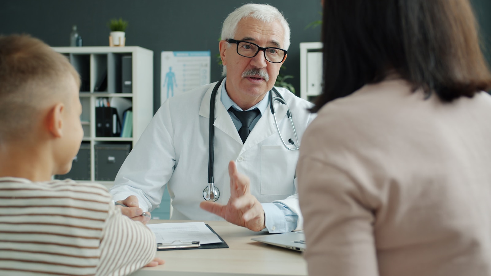 A doctor talking with a patient and her child during a consultation, notes left to the scribe
